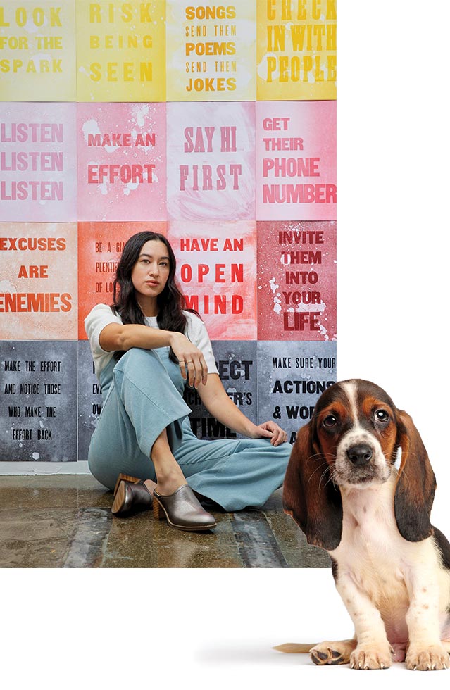 A Basset Hound puppy adorably looking back at you. Female sitting in front of an inspirational wall of signs.